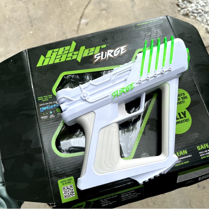 White and green Gel Blaster Surge placed on its packaging box